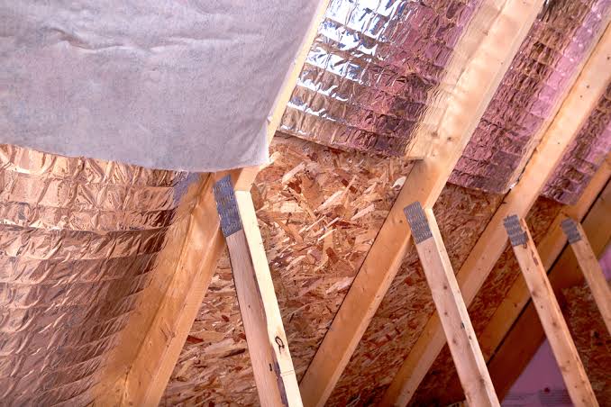 Reflective foil radiant barrier stapled between roof rafters in an attic